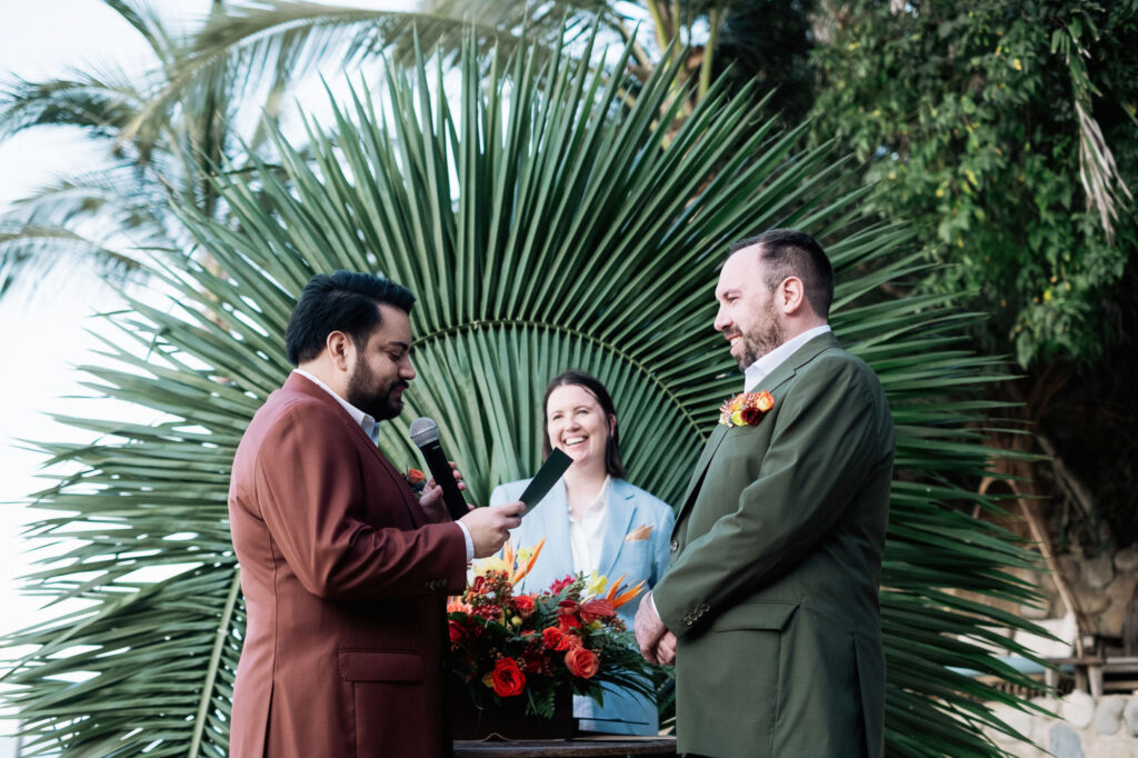 Two grooms exchange vows at outdoor wedding ceremony, Las Caletas Puerto Vallarta, tropical palm backdrop