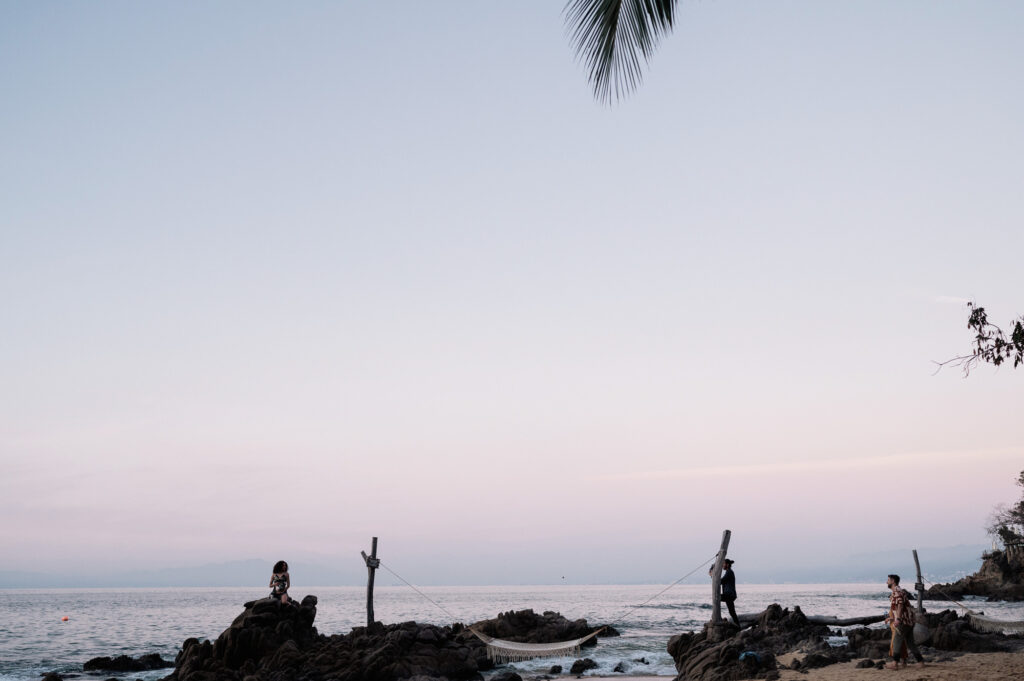 Wedding guests on rocky Las Caletas beach at dusk, hammock between posts, Puerto Vallarta