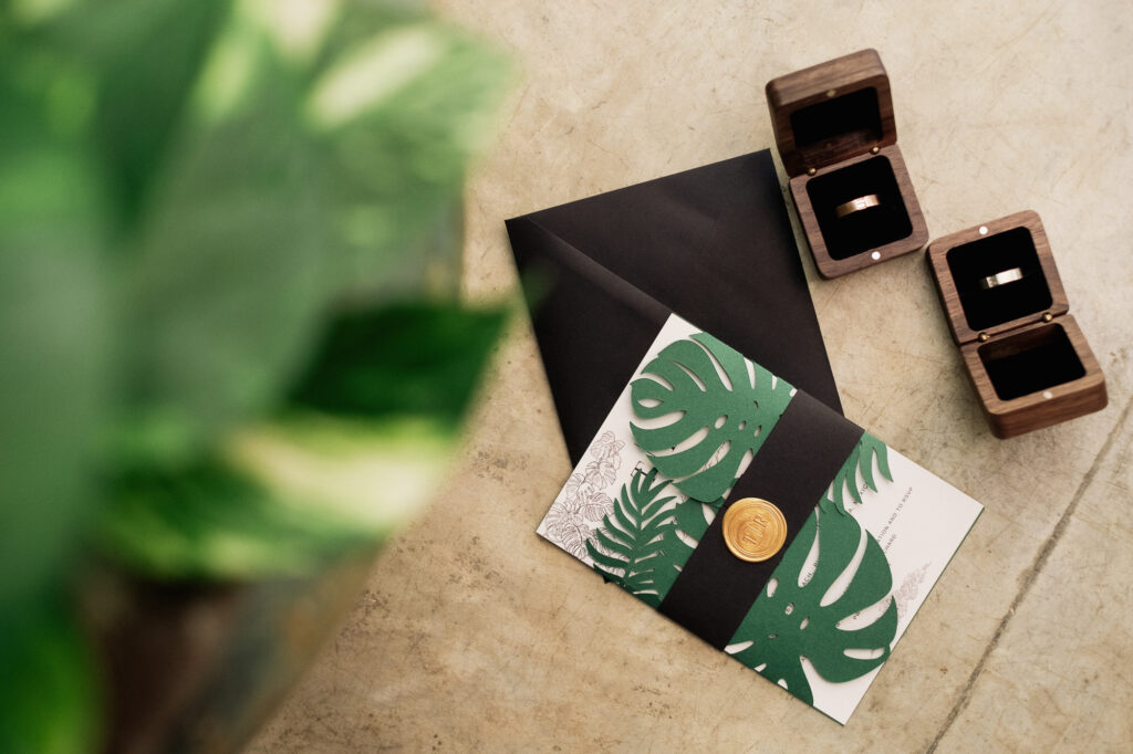 Wedding invitation suite with monstera leaf cutouts and gold wax seal beside wooden ring boxes, Las Caletas Puerto Vallarta