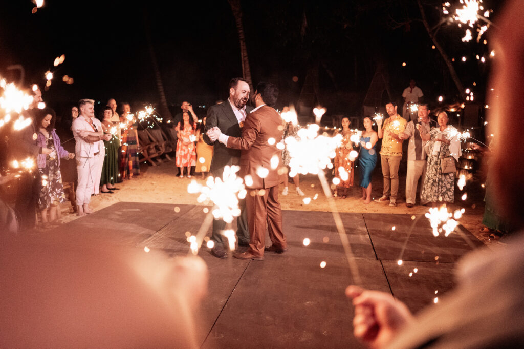 Two grooms share first dance surrounded by sparklers at night, Las Caletas beach wedding reception, Puerto Vallarta