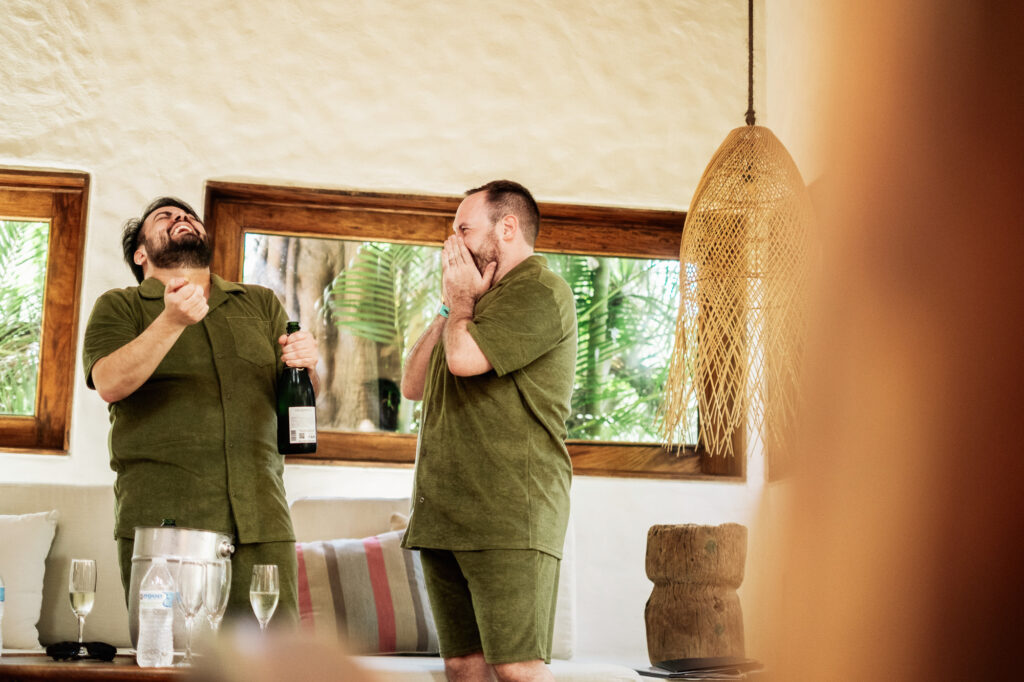 Two grooms laughing with champagne at Las Caletas wedding reception, Puerto Vallarta