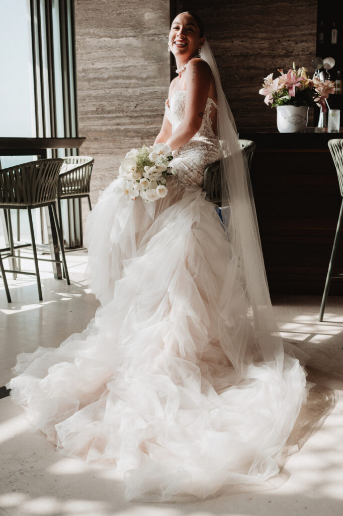 Bride in layered tulle gown holding white bouquet laughing at Hilton Riviera Vallarta wedding