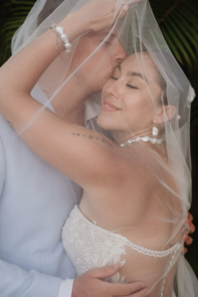 Bride and groom embracing under veil at Hilton Riviera Vallarta wedding, documentary photography by Alex Obregón