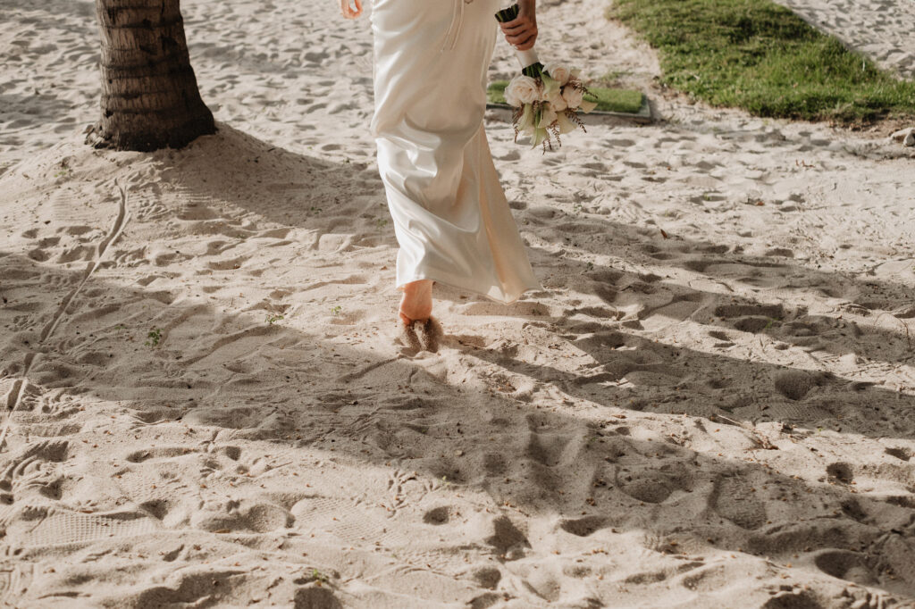 Bride walking barefoot on beach sand holding white bouquet, wedding at St Regis Punta Mita