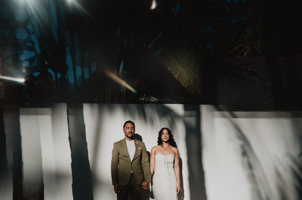 Bride and groom holding hands against white wall with palm shadows, wedding portrait in Sayulita Mexico