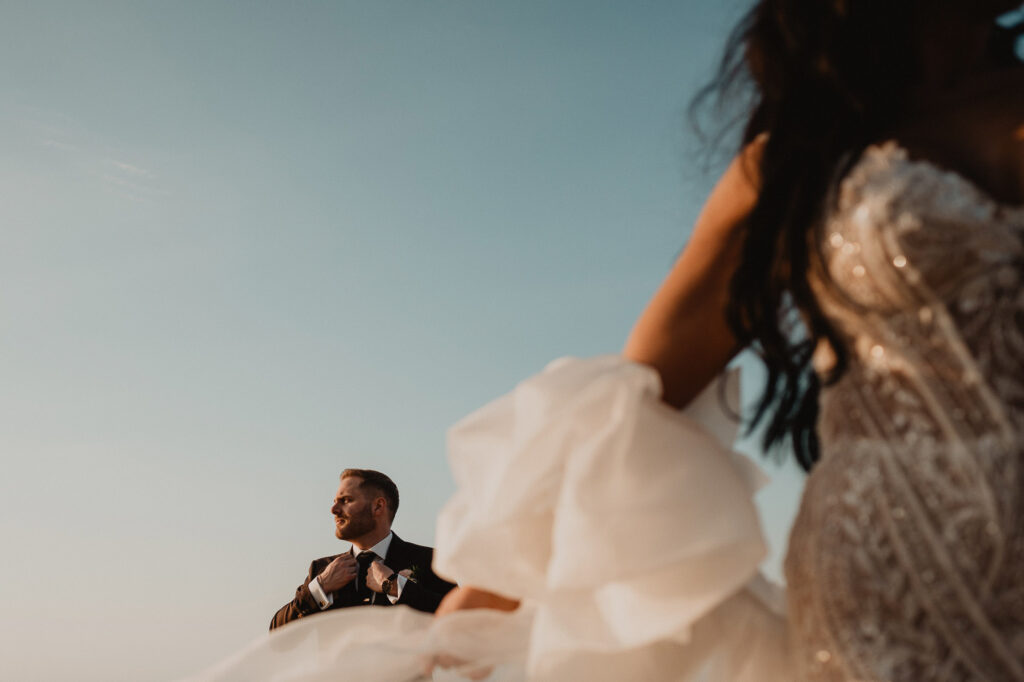 Groom adjusting tie at golden hour wedding at Villa Valentin Sayulita, bride's dress billowing in foreground