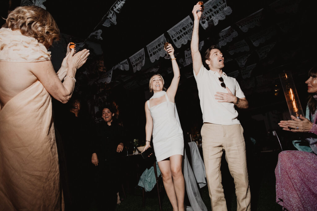 Bride and groom raising glasses at outdoor wedding reception, San Miguel de Allende, papel picado above