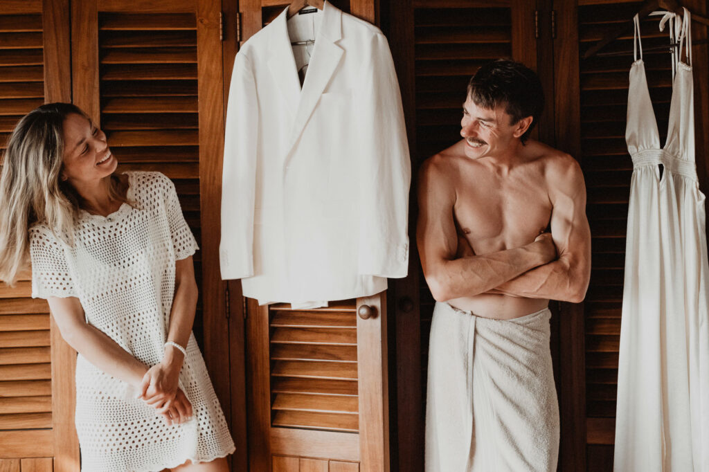 Couple laughing while getting ready for wedding at Villa del Sol Sayulita, white suit and dress hanging nearby