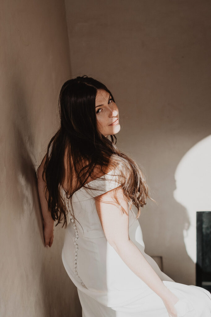 Bride in white gown leaning against wall in warm light, Tulum wedding ceremony, documentary film photography