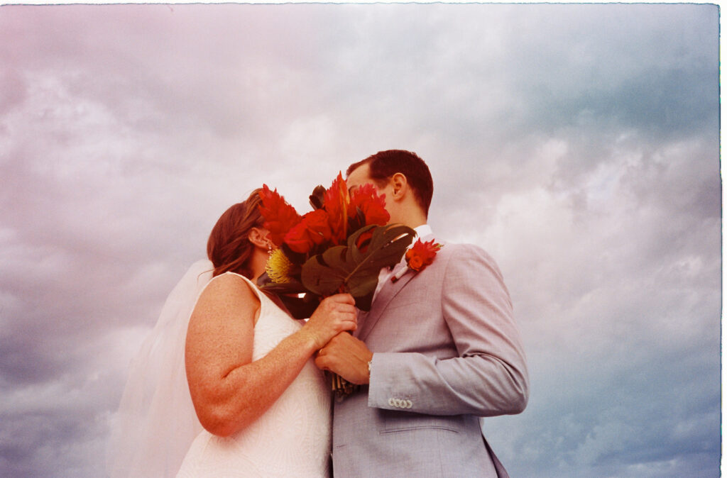 Bride and groom kissing behind red bouquet at Dreams Vista Cancun wedding ceremony, shot on 35mm film