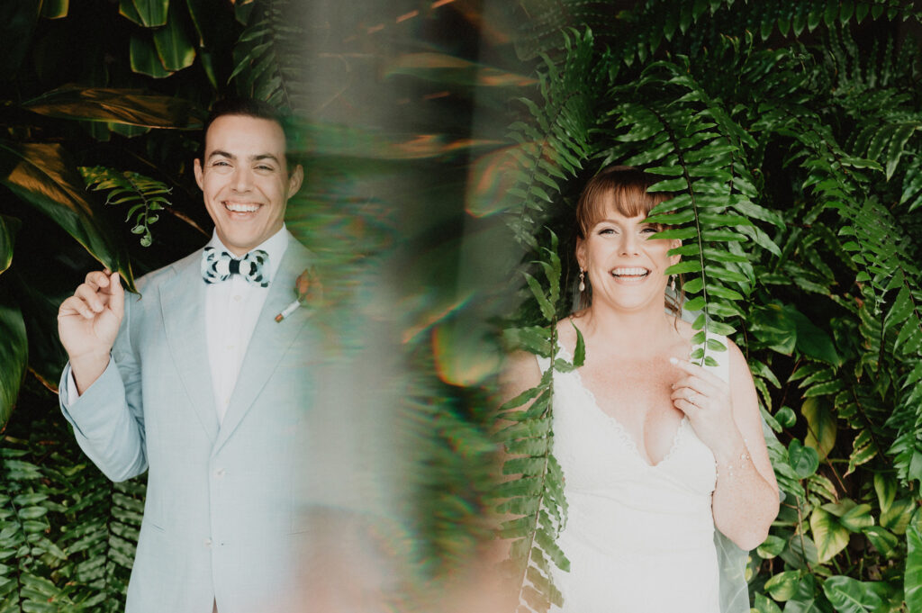 Bride and groom laughing through tropical ferns at Dreams Vista Cancun wedding ceremony, film photography