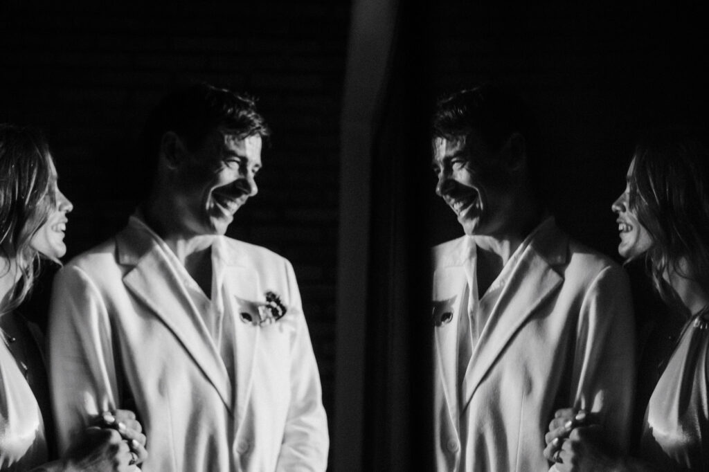 Groom in white suit laughing with bride at Villa del Sol Sayulita wedding reception, black and white film photo