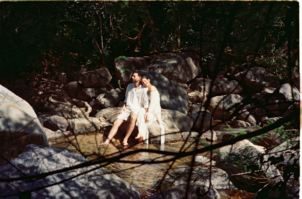 Couple in white sitting on rocks by a jungle stream, engagement session in Puerto Vallarta shot on 35mm film