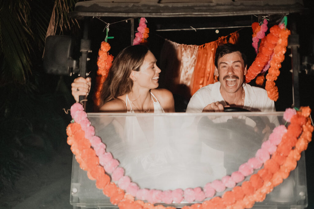 Bride and groom laughing in flower-adorned golf cart at night, Villa del Sol Sayulita wedding reception