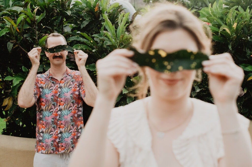 Couple holding tropical leaves over their eyes during engagement session in Sayulita, Mexico