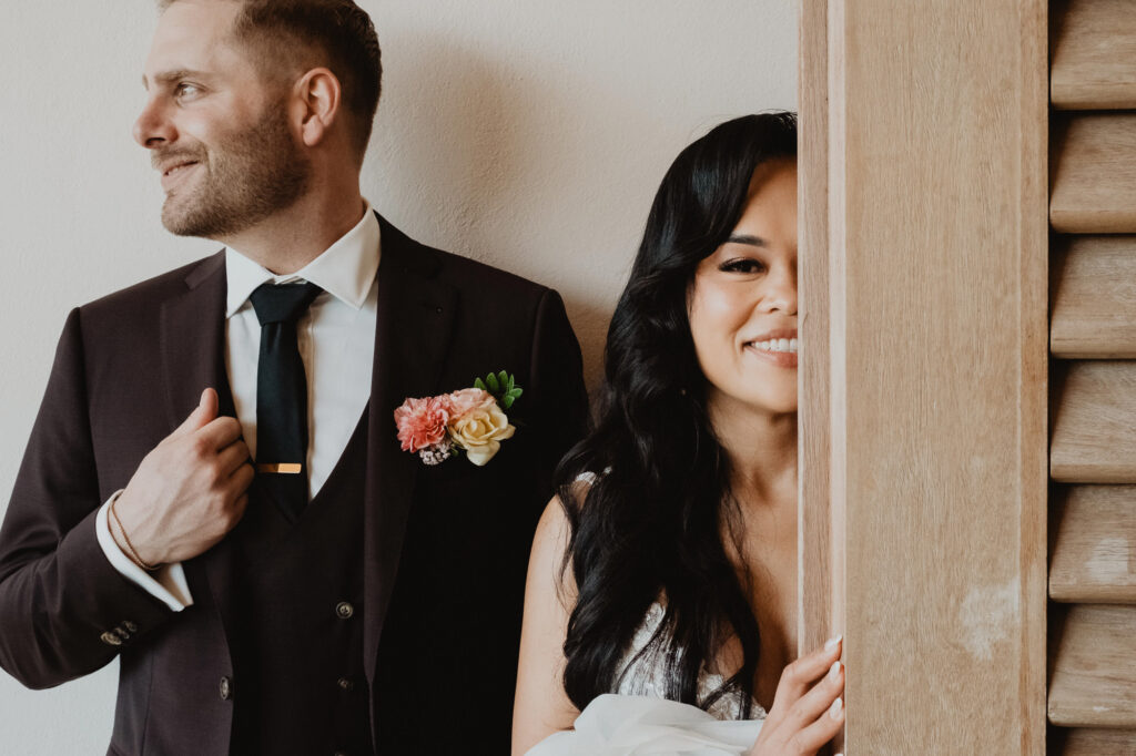 Bride peeks around wooden door smiling at groom in dark suit at Villa Valentin Sayulita wedding