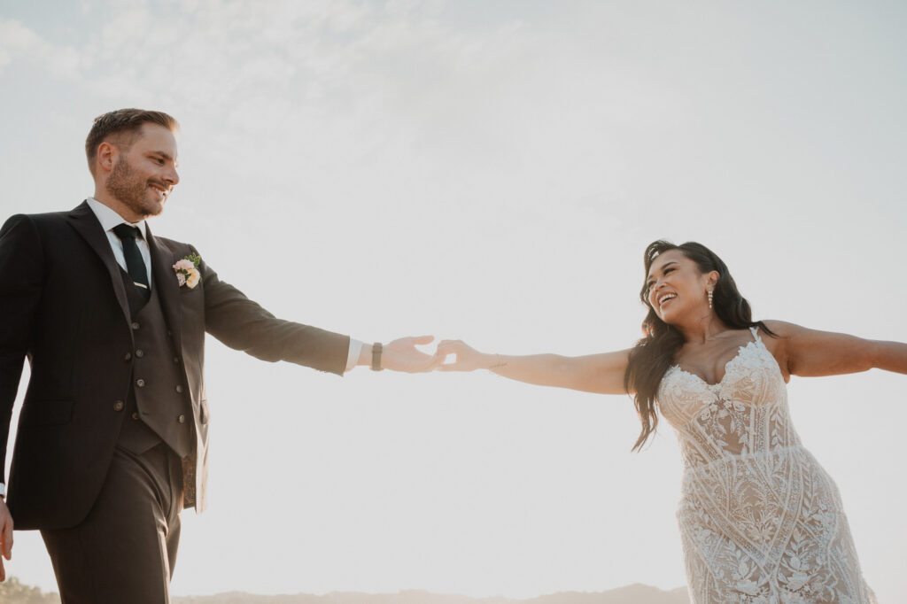 Bride and groom hold hands outdoors at Villa Valentin Sayulita wedding, golden backlight, lace gown and dark suit