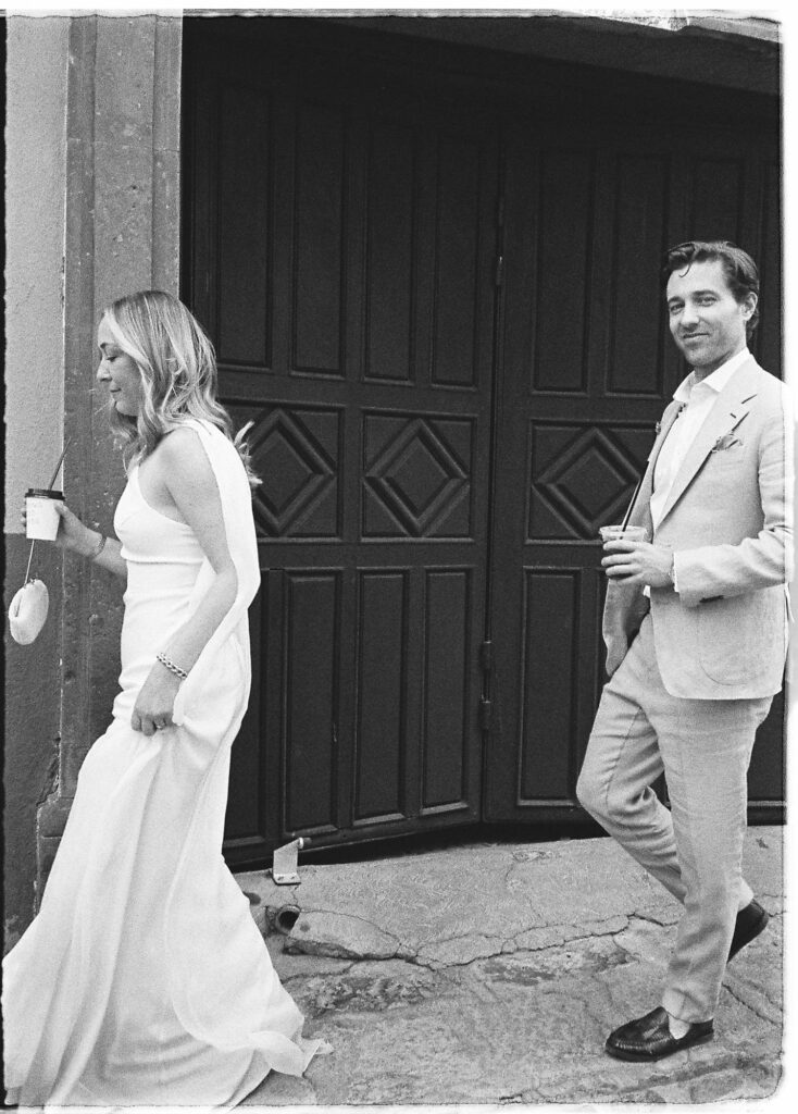 Bride and groom walking past ornate wooden doors in San Miguel de Allende, captured on 35mm film
