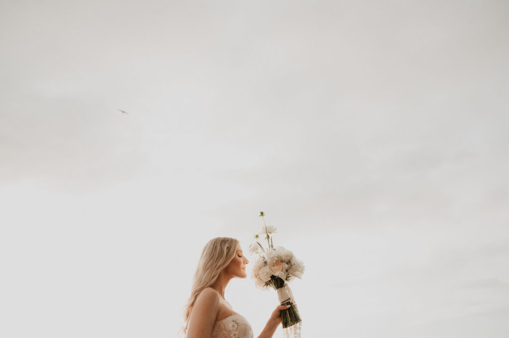 Bride smelling white bouquet against misty sky at One&Only Mandarina elopement, Mexico