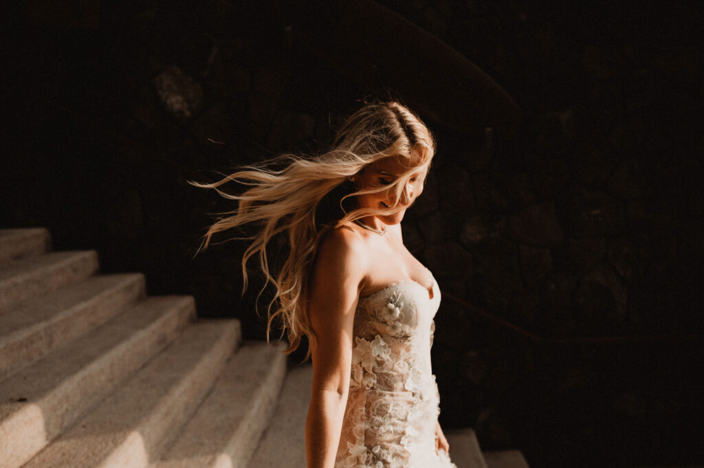 Bride in floral lace gown, hair flowing in the wind on stone steps at One&Only Mandarina elopement