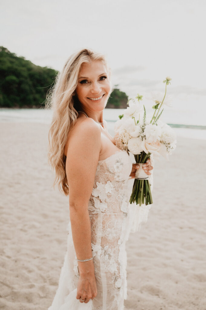 Bride in lace floral gown holding white bouquet on beach at One&Only Mandarina elopement wedding