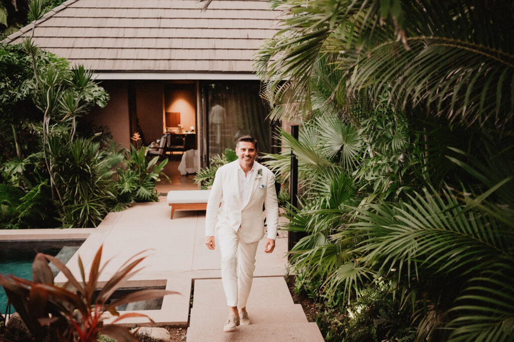 Groom in white linen suit walking through tropical garden at One&Only Mandarina elopement, Mexico