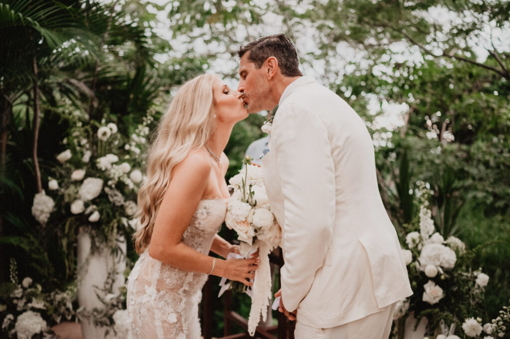 Bride and groom share first kiss at One&Only Mandarina elopement, surrounded by tropical florals
