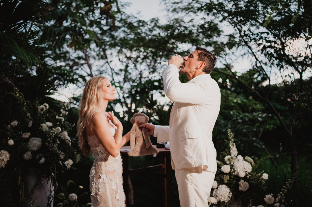 Groom in white suit kisses bride's hand during elopement ceremony at One&Only Mandarina, Mexico