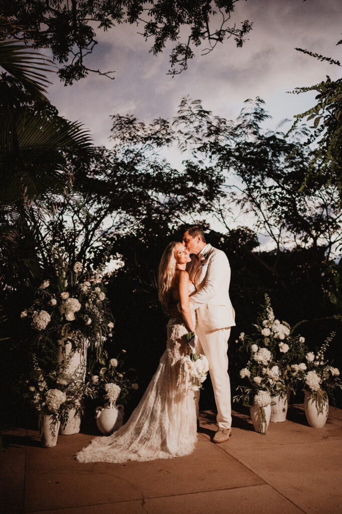 Bride and groom share a kiss at dusk surrounded by white florals at One&Only Mandarina elopement