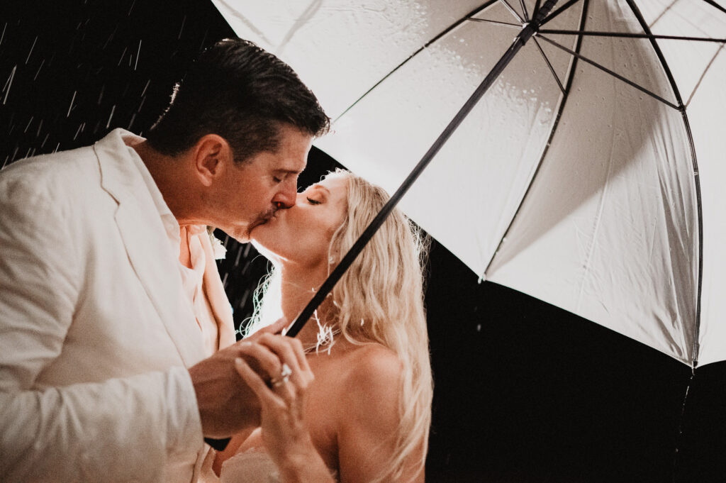 Bride and groom kissing under clear umbrella in the rain at One&Only Mandarina elopement