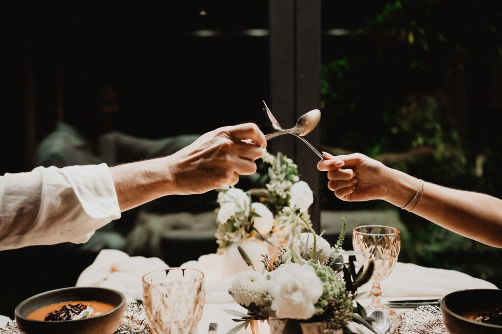 Two hands clinking spoons over a candlelit elopement dinner table at One&Only Mandarina, Mexico