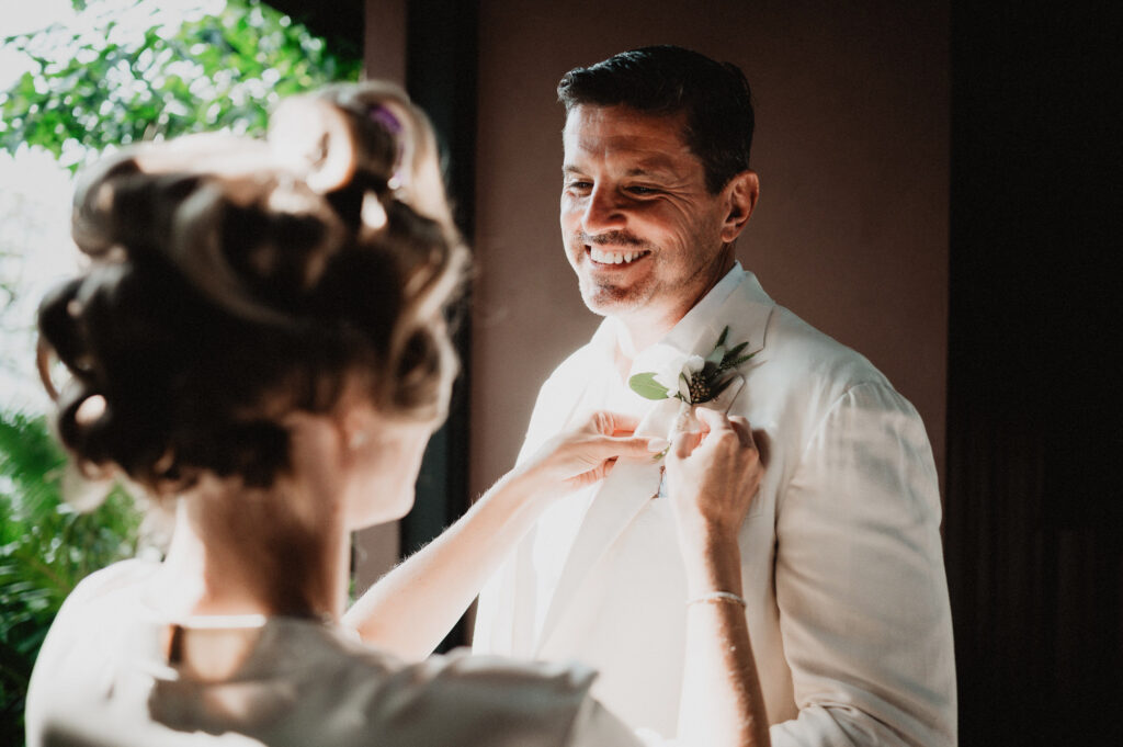 Groom smiling as bride pins boutonniere at One&Only Mandarina elopement, Mexico