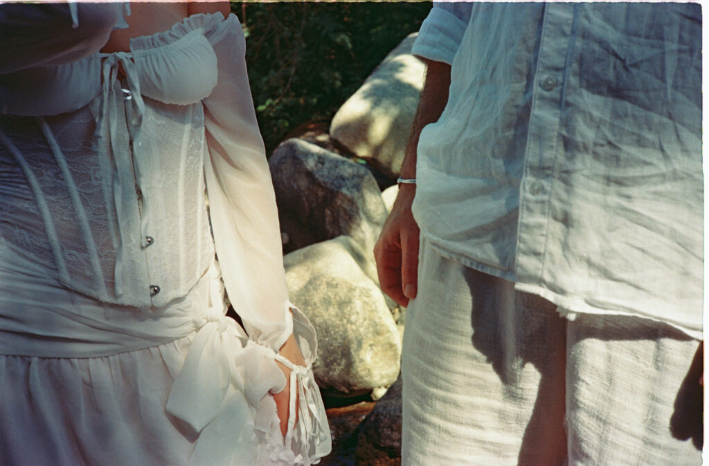 Couple in white linen and lace corset dress standing by rocks, engagement session Puerto Vallarta film photography