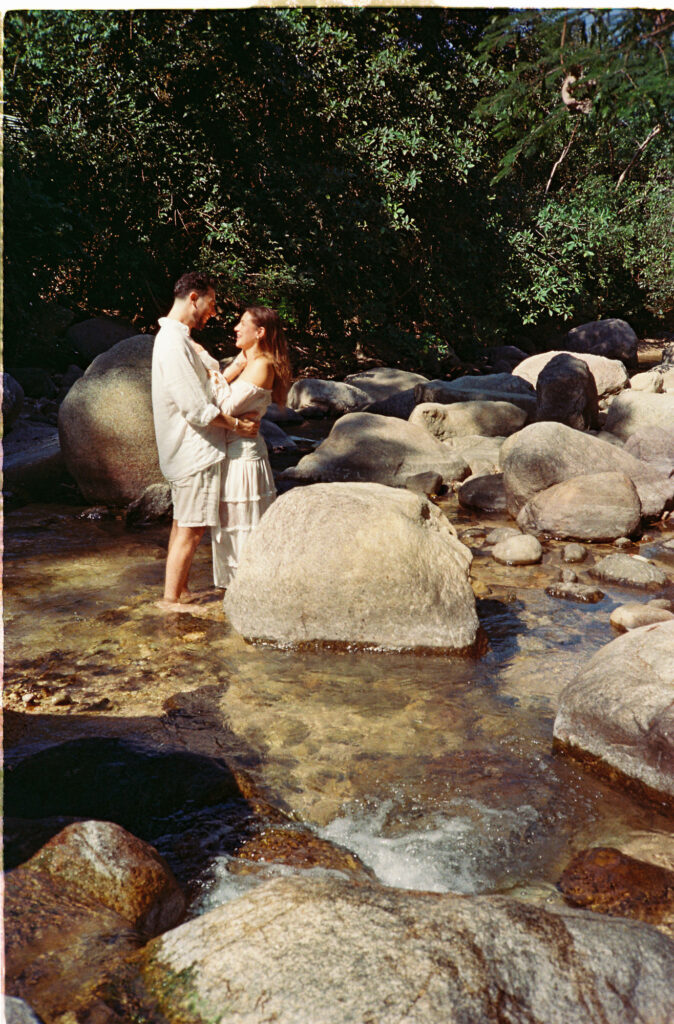 Couple embracing in rocky river stream, engagement session in Puerto Vallarta jungle by film photographer Alex Obregón