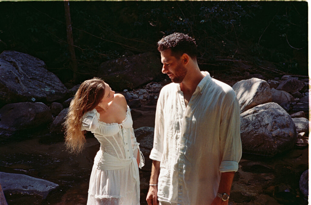 Couple in white outfits sharing a tender moment by a rocky river in Puerto Vallarta engagement session