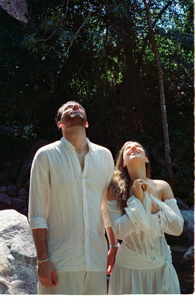 Couple in white linen gazing upward together in sunlit forest, Puerto Vallarta engagement session on 35mm film