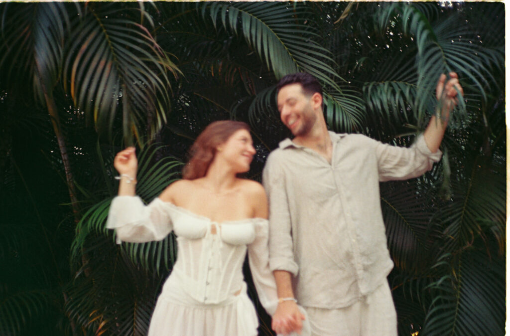 Couple dancing and laughing among tropical palms during engagement session in Puerto Vallarta, shot on 35mm film
