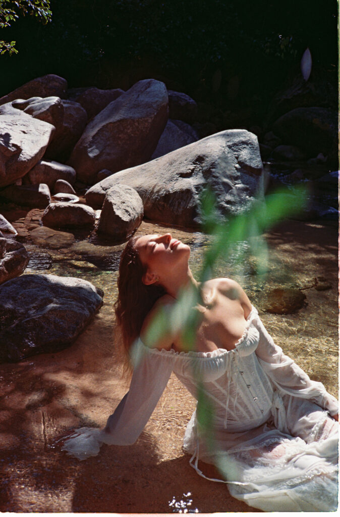Woman in white corset gown sits in rocky stream, Puerto Vallarta engagement session by Alex Obregón