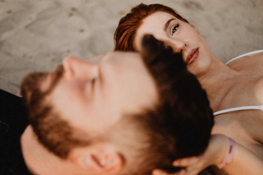 Couple lying on beach sand in Puerto Vallarta engagement session, woman with red hair gazing upward