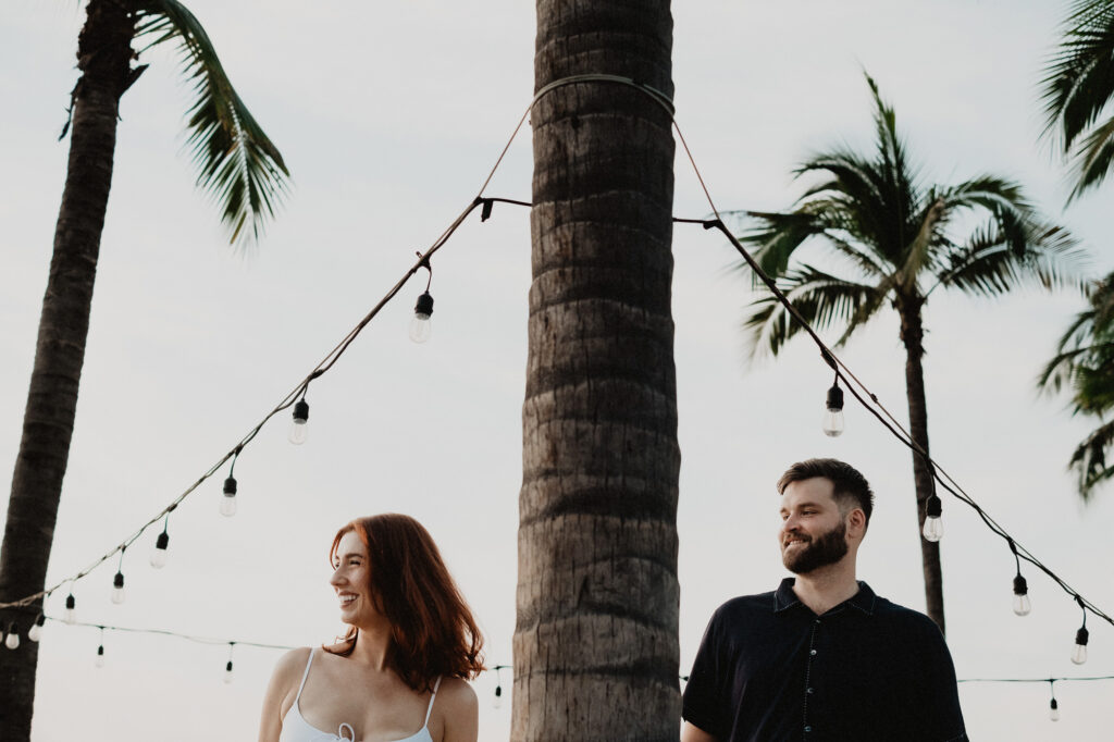Couple laughing under string lights and palm trees during engagement session in Puerto Vallarta
