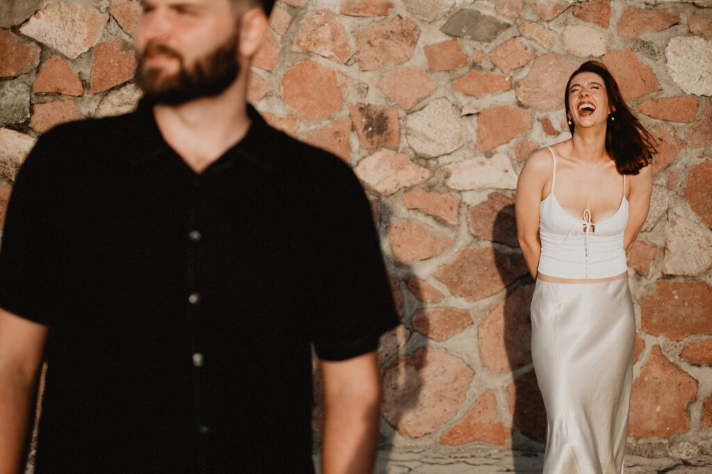 Woman laughing joyfully against stone wall during engagement session in Puerto Vallarta, man in foreground
