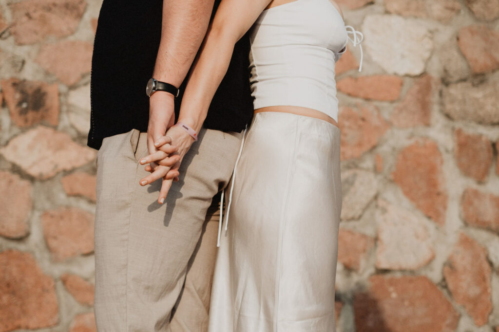 Couple holding hands during engagement session in Puerto Vallarta, stone wall background, warm natural light