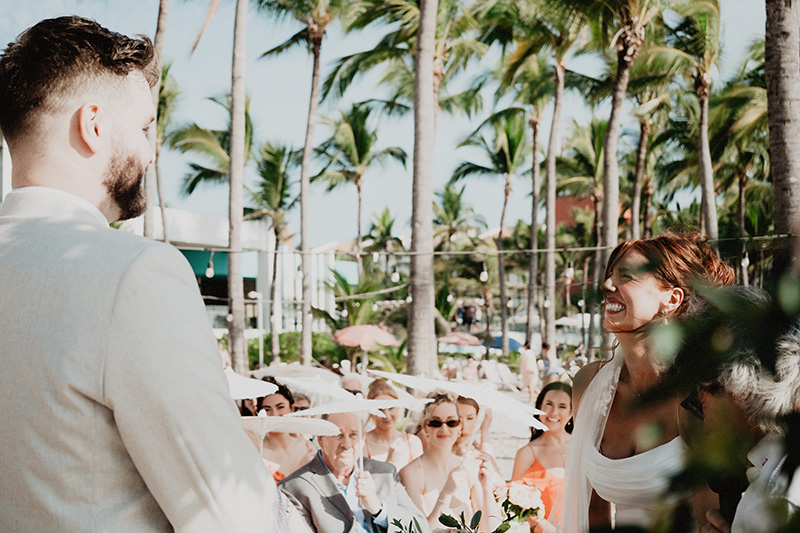 Bride laughing during wedding ceremony at Riu Vallarta with guests and palm trees in background