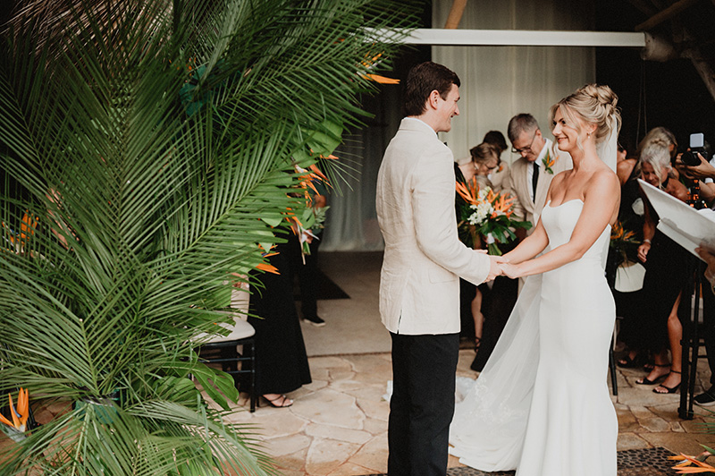 Bride and groom hold hands during wedding ceremony at Casa Cosmos, Puerto Vallarta, surrounded by tropical blooms