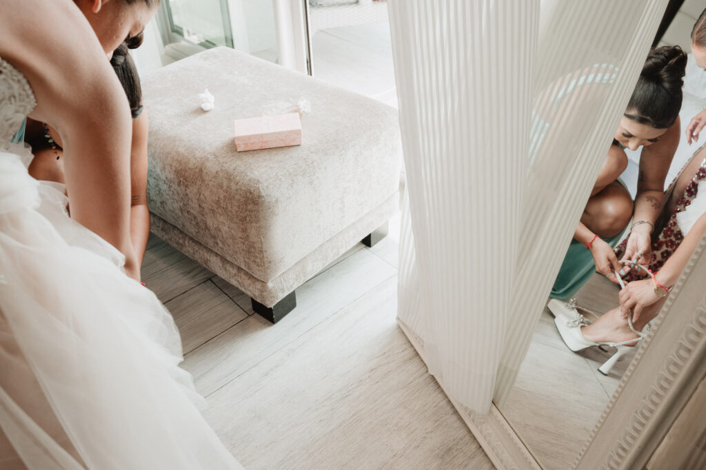 Bride getting shoes fastened by bridesmaid in mirror reflection, wedding prep at Hilton Puerto Vallarta