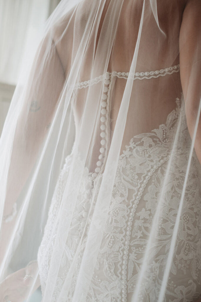 Close-up of lace wedding gown back with pearl buttons and veil, bridal detail at Hilton Puerto Vallarta