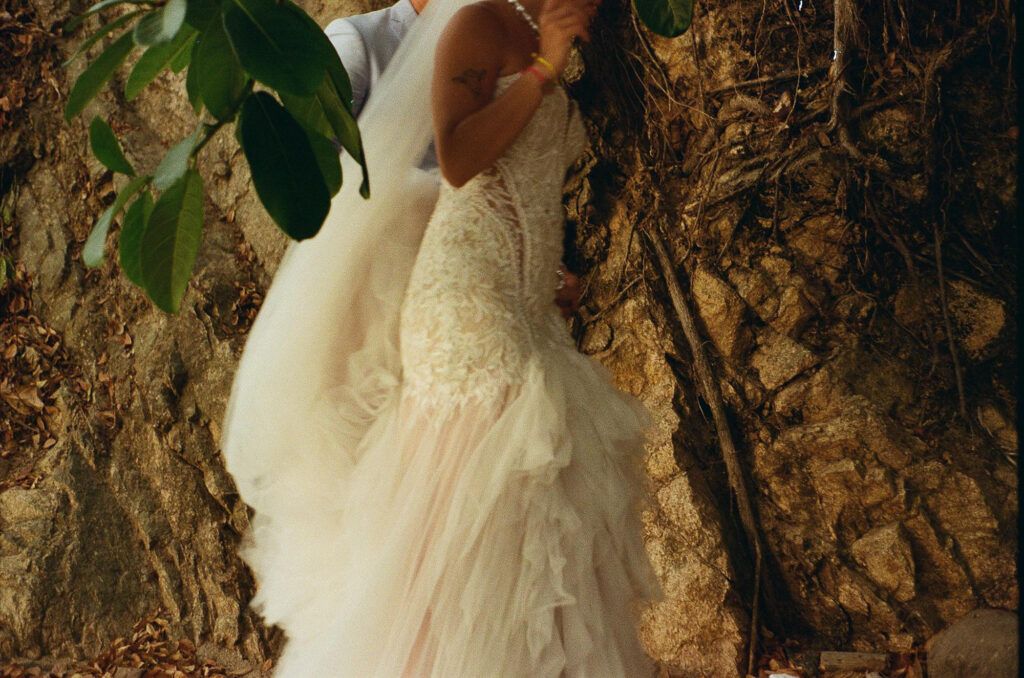 Bride in lace gown embraced by groom against rocky cliffside at Hilton Puerto Vallarta wedding