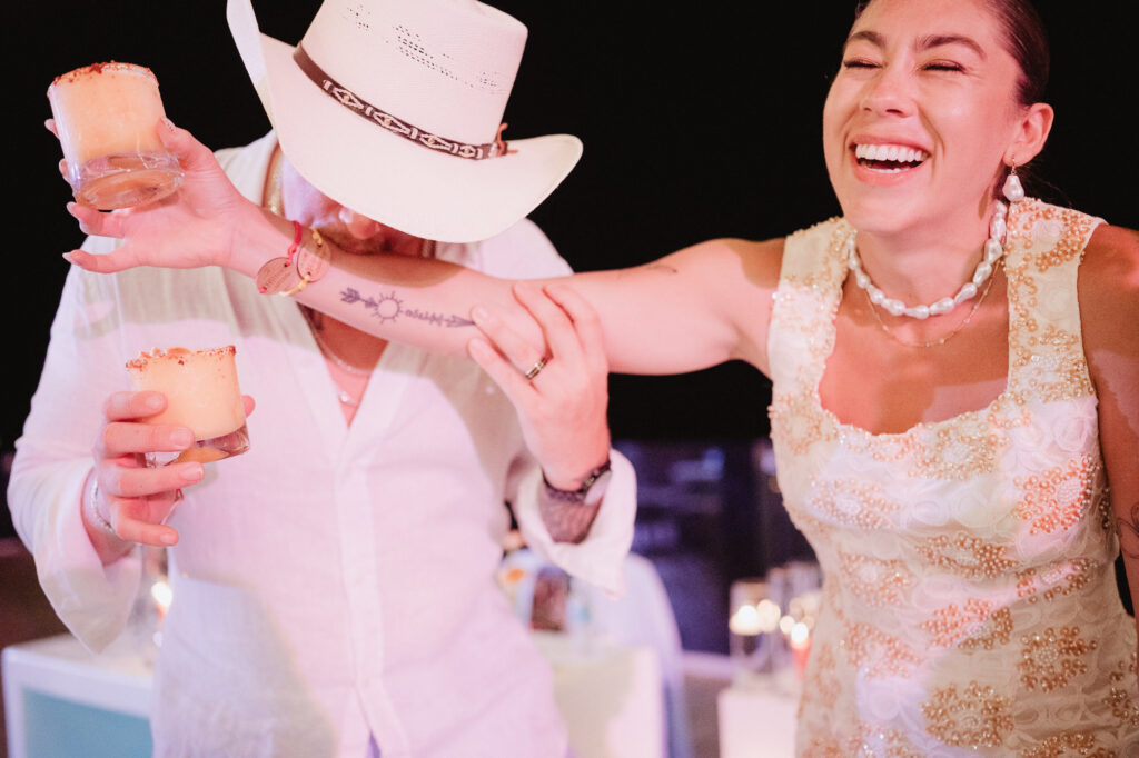 Bride laughing with partner holding cocktails at Puerto Vallarta wedding reception, documentary style