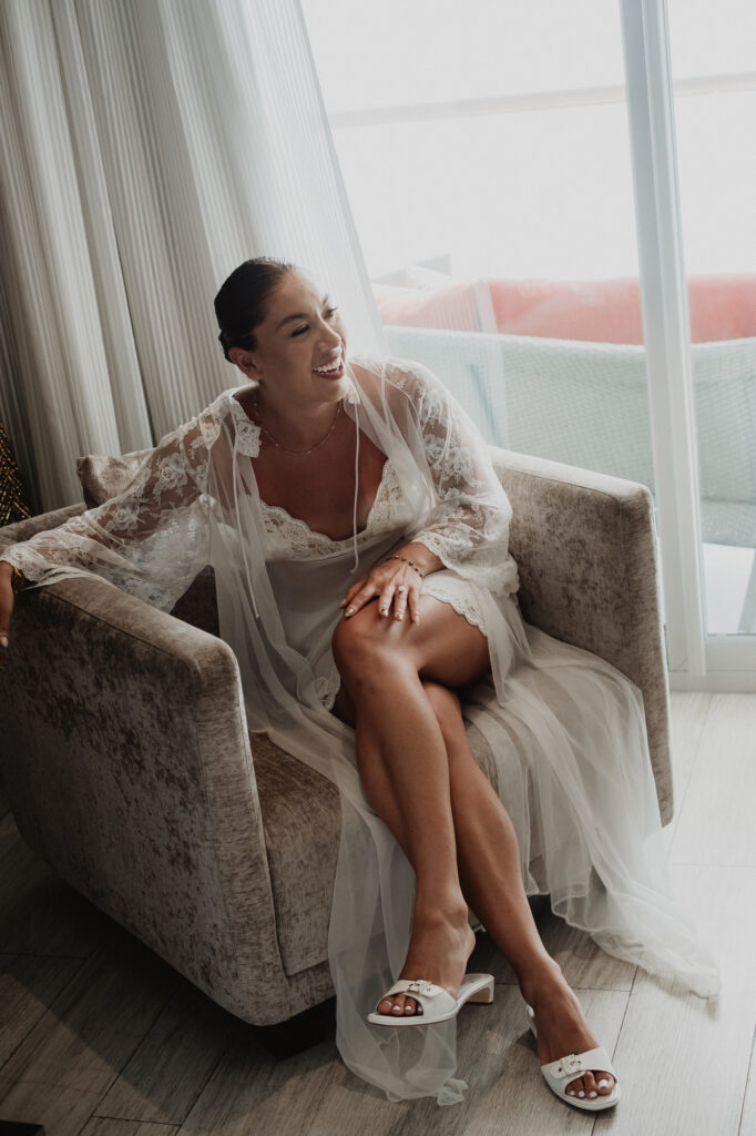 Bride in lace robe laughing in armchair at Hilton Puerto Vallarta wedding morning preparation