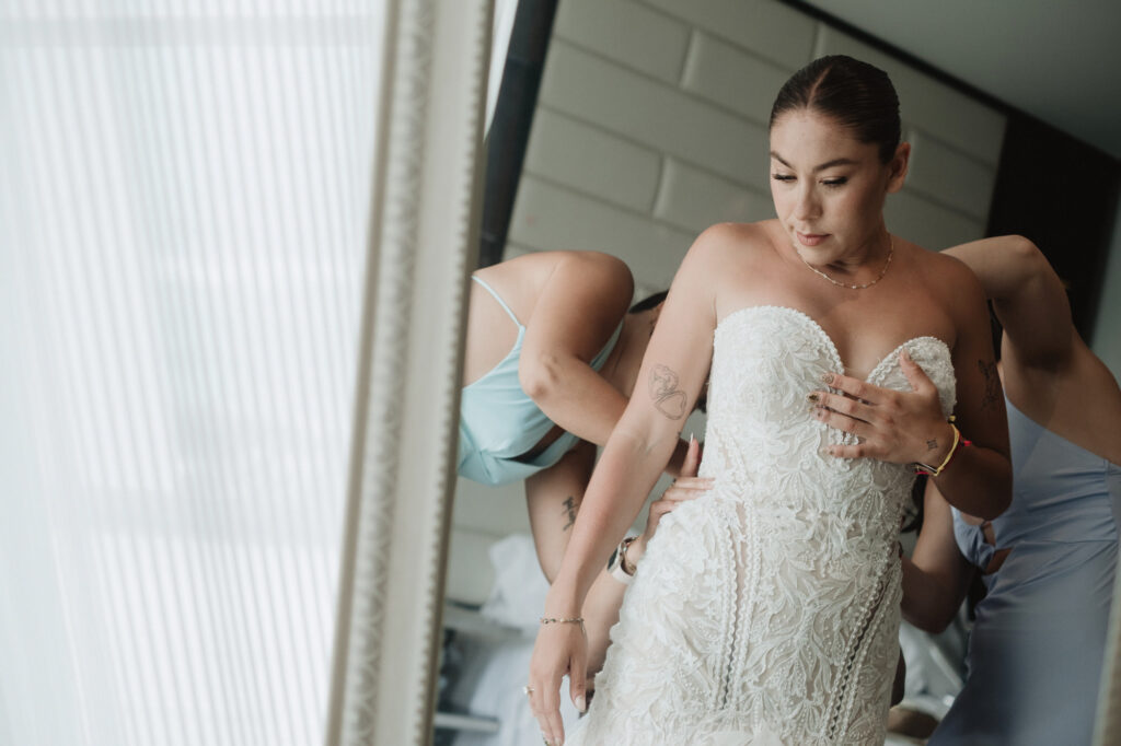 Bride being helped into lace wedding gown by bridesmaids, getting ready at Hilton Puerto Vallarta